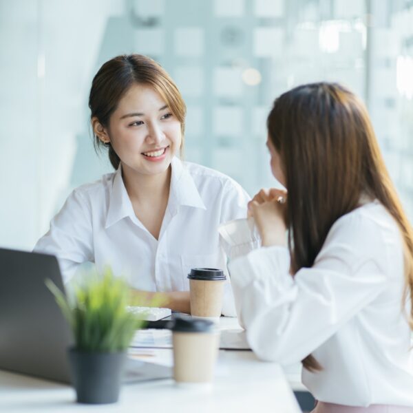 Two people sitting around a laptop and talking.